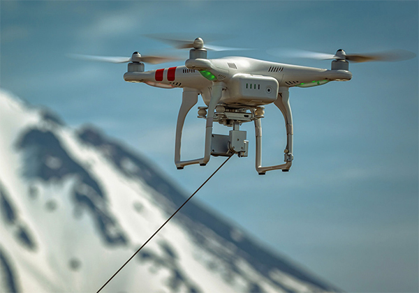 Ilustracja przedstawiająca drony, które mogą pozostawać w powietrzu przez długi czas, korzystając z zasilania dostarczanego przez system uwięzi